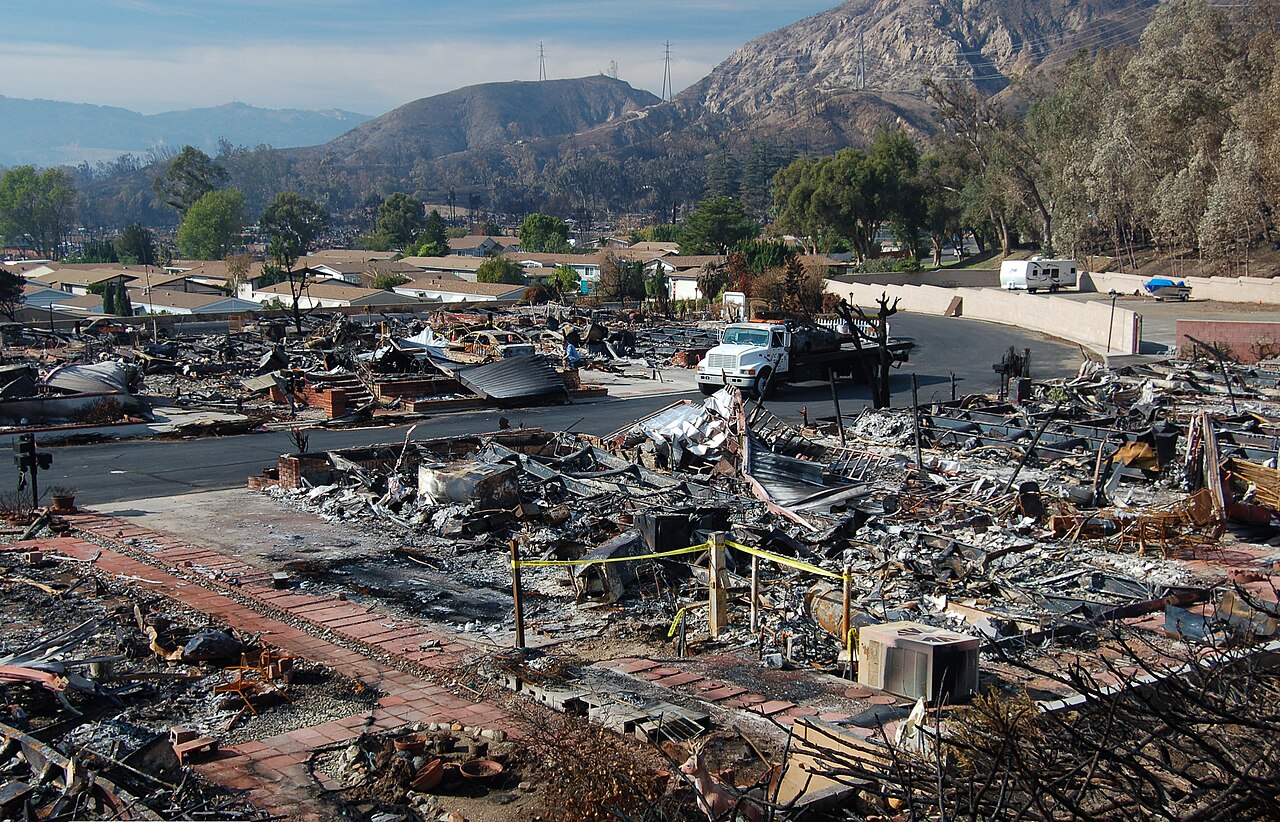 A residential street after a wildfire, with cleared foundations and burned debris where houses stood.